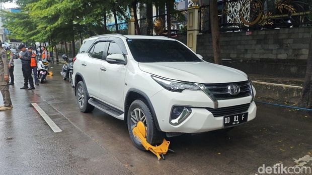 Mobil yang parkir di badan Jalan Boulevard Makassar digembok. Mobil yang parkir di badan Jalan Boulevard Makassar digembok.