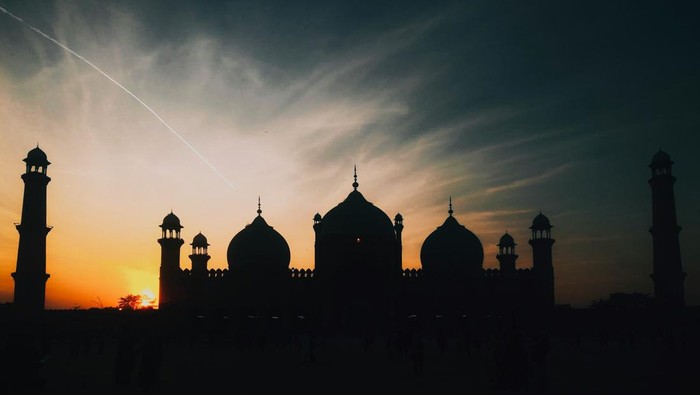 Siluet hitam masjid dengan latar belakang langit sore.