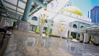 Seorang jamaah tampak sedang mengambil wudhu dengan berlatar belakang bangunan masjid.