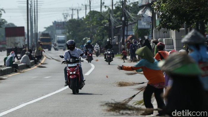 Sejumlah warga duduk di pinggir jalan Pantura, Sabtu (14/3/2026). Sambil membawa sapu lidi, berharap pengendara yang melintas melemparkan uang