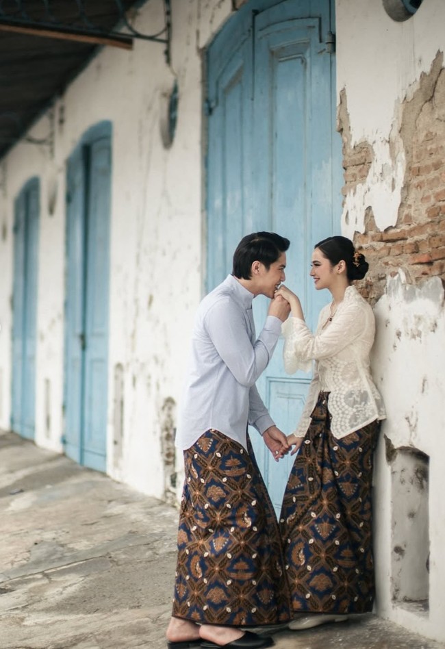 Pemotretan dilakukan di depan bangunan rumah bergaya klasik dengan ornamen ukiran khas. Atap tua dan detail arsitekturnya memberikan nuansa heritage yang memperkuat konsep tradisional. Foto: Instagram/@thebridestory