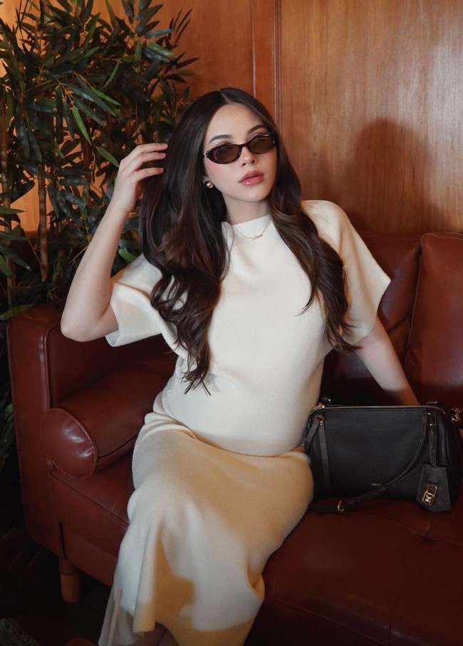 Alyssa terlihat mengenakan dress panjang berwarna cream yang memiliki potongan sederhana namun elegan. Dress tersebut memiliki siluet lurus yang mengikuti bentuk tubuhnya, sehingga baby bump yang semakin besar terlihat jelas namun tetap memberi kesan anggun. Foto: Instagram/@alyssadaguise