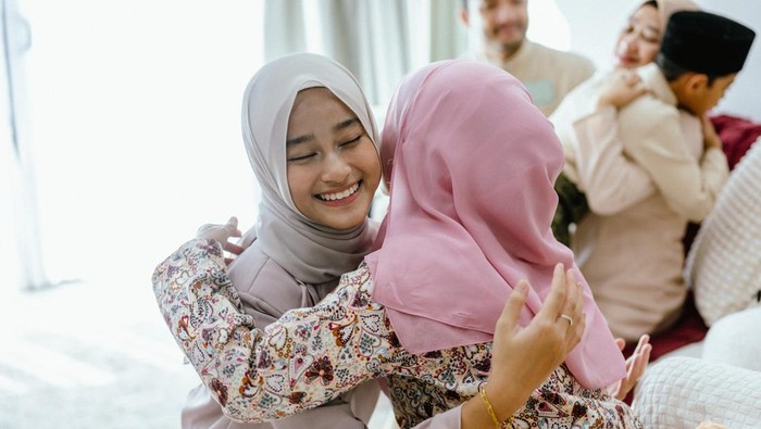 A young teenage girl receiving blessings from her parents during the festival of Hari Raya Aidilfitri. A Malay Muslim family portrait for Eid Mubarak/Hari Raya Aidilfitri in the living room.