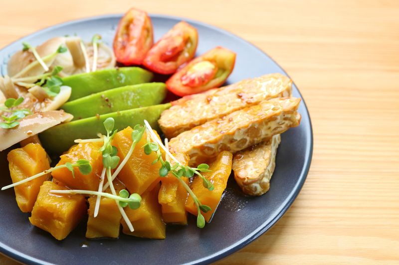 Plate of Pan fried Tempeh and Colorful Vegetables Salad Garnished with Daikon Sprouts