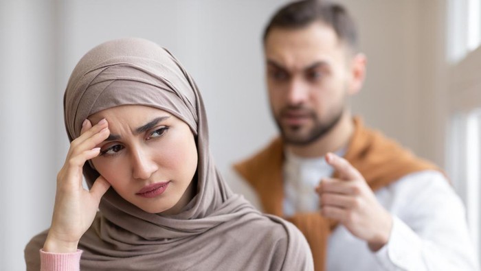 Husband Shouting At Depressed Wife Tired Of Domestic Violence And Victimization Standing At Home. Selective Focus. Relationship With Abuser And Family Conflicts