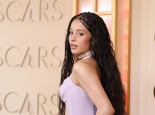 Aktris Chase Infiniti tampil menonjol dengan wavy knotless box braids yang dibelah tengah. Gaya rambut panjang ini memberi kesan feminin sekaligus bebas bergerak. Riasannya juga tak kalah menarik. Eyeshadow dusty lavender yang dikenakan dibuat senada dengan gaunnya, menciptakan tampilan monokrom yang elegan. Foto: Penske Media via Getty Images/Penske Media