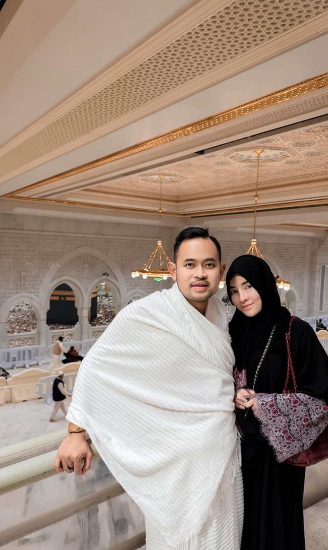 Shandy Purnamasari dan Gilang Widya Pramana tampil serasi dalam suasana penuh kekhusyukan saat menjalani ibadah umrah menjelang malam-malam terakhir Ramadan 2026. Keduanya berpose dengan latar belakang kemegahan arsitektur Masjidil Haram dan pemandangan Kabah yang ikonik. Foto: Dok. Instagram @juragan_99 & @shandypurnamasari.