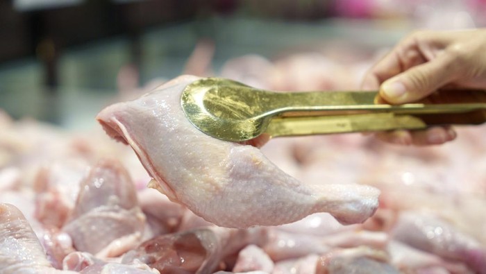 Close-up of a shopper using golden tongs to select fresh chicken pieces at a local market, showcasing freshness and ingredient quality.