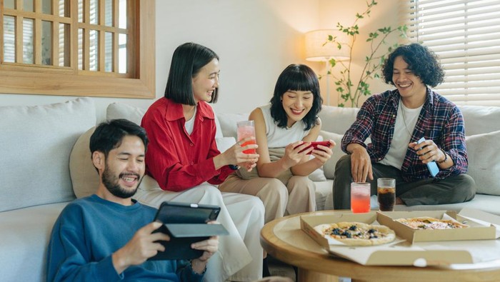 Group of friends enjoying life and having fun at home. Friends day in the apartment. Young women and young men spending time together chatting and making activities in the living room. Concept about lifestyle