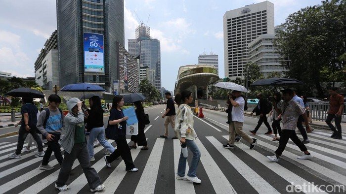Pekerja melintasi pelican crossing Tosari, Jalan MH Thamrin, Jakarta, Selasa (17/3/2026), dengan menggunakan payung untuk menghindari terik matahari. Suhu di Jakarta tercatat mencapai 35,6 derajat Celsius.