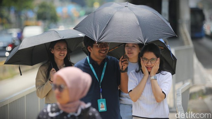 Pekerja melintasi pelican crossing Tosari, Jalan MH Thamrin, Jakarta, Selasa (17/3/2026), dengan menggunakan payung untuk menghindari terik matahari. Suhu di Jakarta tercatat mencapai 35,6 derajat Celsius.