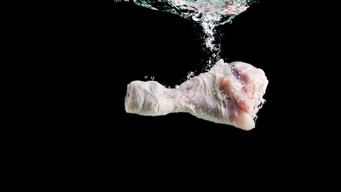 Chicken leg falls into the water on a black background, washing meat before cooking and eating