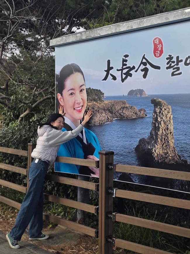 Unggahan foto Instagram-nya sontak membangkitkan nostalgia penonton Jewel in the Palace dari penjuru dunia. Lee Young Ae tampil dengan gaya kasual memakai jaket abu-abu dan denim jeans, tersenyum lebar memeluk billboard yang menampilkan fotonya sebagai Dae Jang Geum dan pemandangan Oedolgae. Foto: dok. Instagram @leeyoungae0824