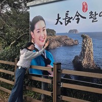 Unggahan foto Instagram-nya sontak membangkitkan nostalgia penonton Jewel in the Palace dari penjuru dunia. Lee Young Ae tampil dengan gaya kasual memakai jaket abu-abu dan denim jeans, tersenyum lebar memeluk billboard yang menampilkan fotonya sebagai Dae Jang Geum dan pemandangan Oedolgae. Foto: dok. Instagram @leeyoungae0824