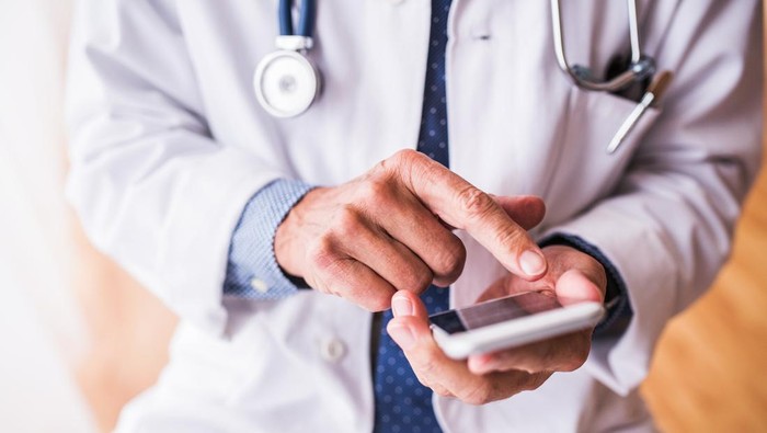 Unrecognizable senior male doctor with smartphone at the office, text messaging.
