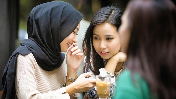 Muslim female whispering a secret to her friend as they sip on Malaysian milk tea at a Kuala Lumpur street side cafe.