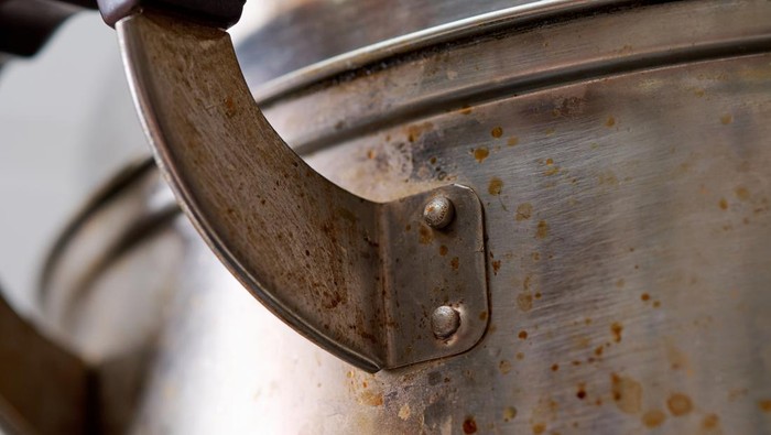 Metal cooking pot showing handle, rivets, and many grease stains after use