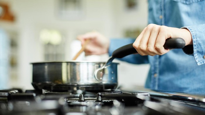 Midsection image of woman stirring food in cooking pan. Utensil is placed on gas stove. Female is holding handle of frying pan. She is preparing food in domestic kitchen.