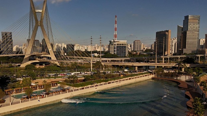 A drone view shows a person surfing at an artificial wave pool as cars pass along the Marginal Pinheiros highway, with the Estaiada Bridge in the background, in Sao Paulo, Brazil, March 20, 2026. REUTERS/Amanda Perobelli