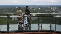 Pengunjung berjalan di atas jembatan kaca. Terdiri dari dua orang dewasa dan dua anak-anak.