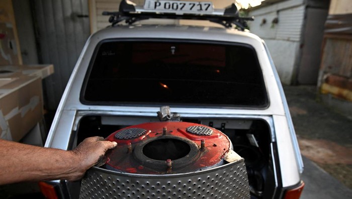 Cuban mechanic Juan Carlos Pino, 56 and his nephew put charcoal into a welded fuel tank to fuel Pino's modified 1980 Polish‑built Polski car, adapted to run on charcoal, a cheaper and more abundant alternative to gasoline since the United States cut off oil shipments to the Caribbean island, in Aguacate, Cuba, March 16, 2026. REUTERS/Norlys Perez