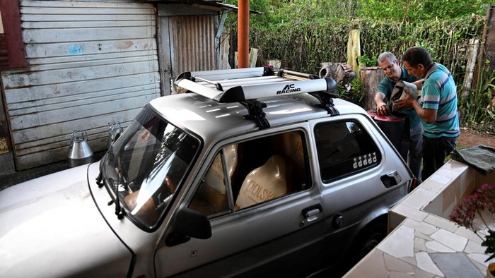 Cuban mechanic Juan Carlos Pino, 56 and his nephew put charcoal into a welded fuel tank to fuel Pino's modified 1980 Polish‑built Polski car, adapted to run on charcoal, a cheaper and more abundant alternative to gasoline since the United States cut off oil shipments to the Caribbean island, in Aguacate, Cuba, March 16, 2026. REUTERS/Norlys Perez