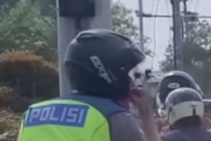 Pria berseragam polisi ngerokok di motor.