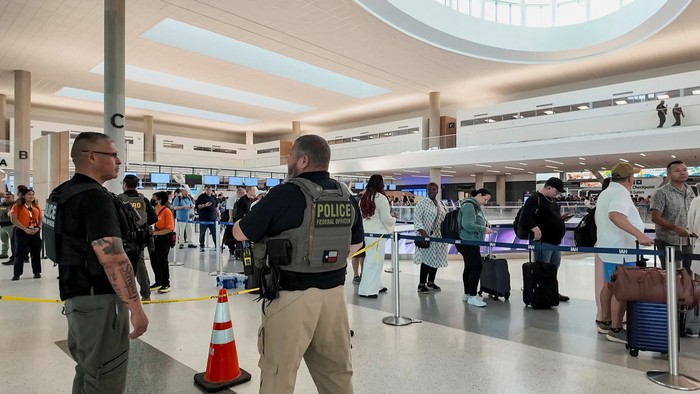 Two Immigration and Customs Enforcement (ICE) agents observe passengers waiting in long TSA lines