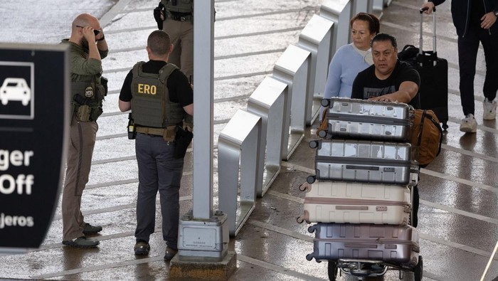 An Immigration and Customs Enforcement (ICE) agent observes passengers wait in long TSA lines amid a funding standoff that has forced 50,000 airport security officers to go without pay, causing delays at airports, at the George Bush Intercontinental Airport in Houston, Texas, U.S., March 25, 2026.    REUTERS/Antranik Tavitian
