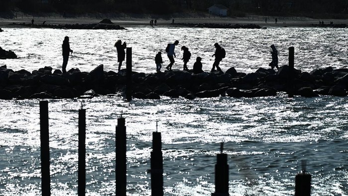 Tourists are silhouetted on a mole as rescuers try to refloat a stranded 10-meter-long humback back into the Baltic Sea at Timmendorfer Strand beach near Travemuende, northern Germany, March 26, 2026. REUTERS/Jonas Walzberg