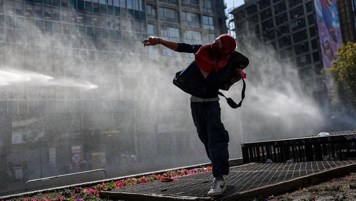 A demonstrator throws an object as a water cannon is used during a protest against the Chilean government's budget cuts to education, in Santiago, Chile, March 26, 2026. REUTERS/Pablo Sanhueza