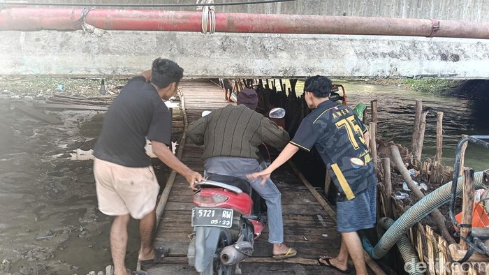 Seorang pengendara melintasi jalan kolong jembatan dibantu dua orang relawan.