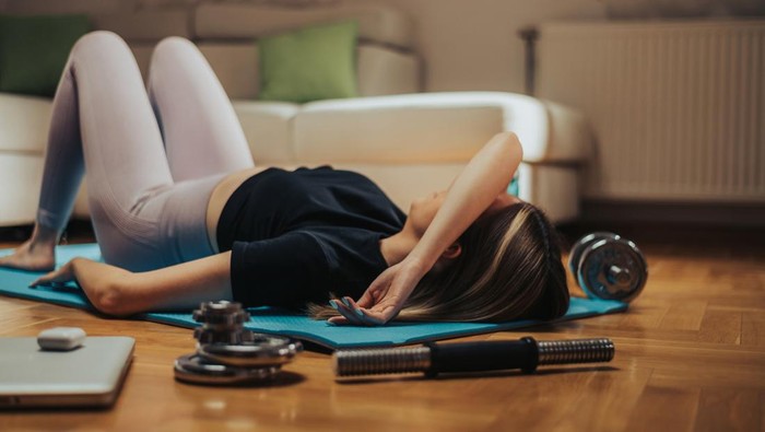 Attractive young woman lying on the floor exhausted after her training with dumbbells at home