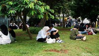  Sejumlah orang tampak bersantai di area rumput Taman Literasi. Beberapa pasangan terlihat duduk bersama menikmati suasana.