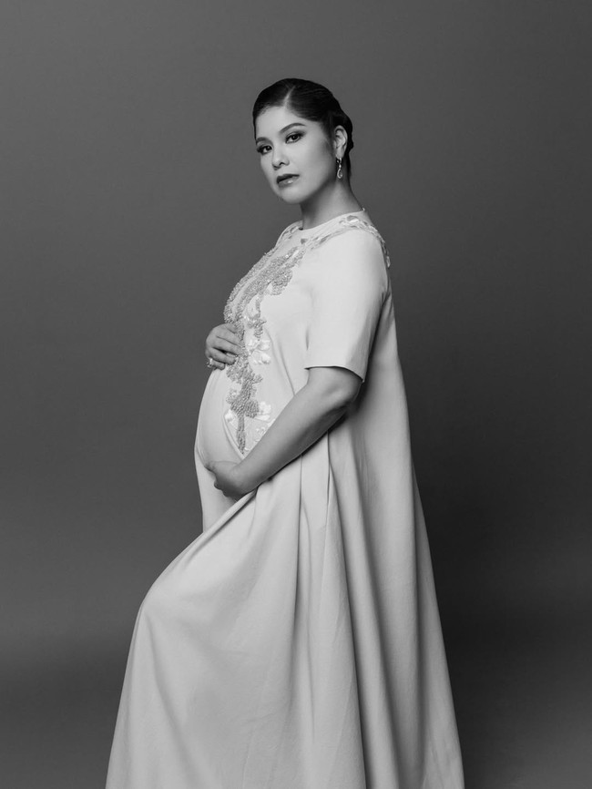 Pemotretan kehamilan lainnya masih dalam nuansa hitam-putih, namun Annisa tampak lebih glamor. Mantan model dan aktris ini memakai maxi dress berhias bordir. Rambutnya disanggul bergaya modern dan dipercantik aksesori seperti anting dan cincin. Foto: Instagram/@annisayudhoyono