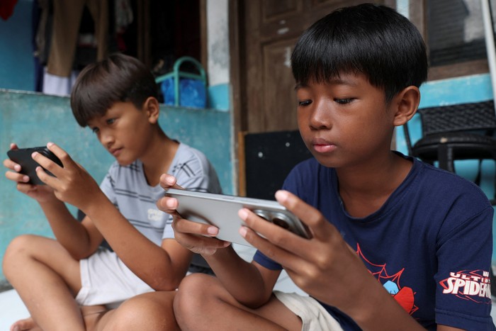 Affan Haritsah, 11, Daffa Ibnu Alkhalifi, 12, and Kevin Prince, 14, use their phones, as Indonesias communications and digital information ministry implements restrictions against high-risk social media platforms, including Facebook, TikTok, and R