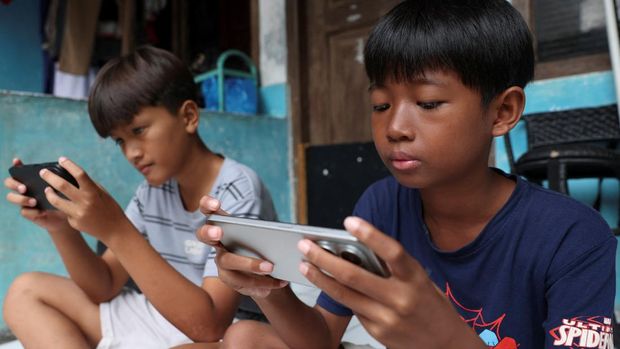 Affan Haritsah, 11, Daffa Ibnu Alkhalifi, 12, and Kevin Prince, 14, use their phones, as Indonesia's communications and digital information ministry implements restrictions against 