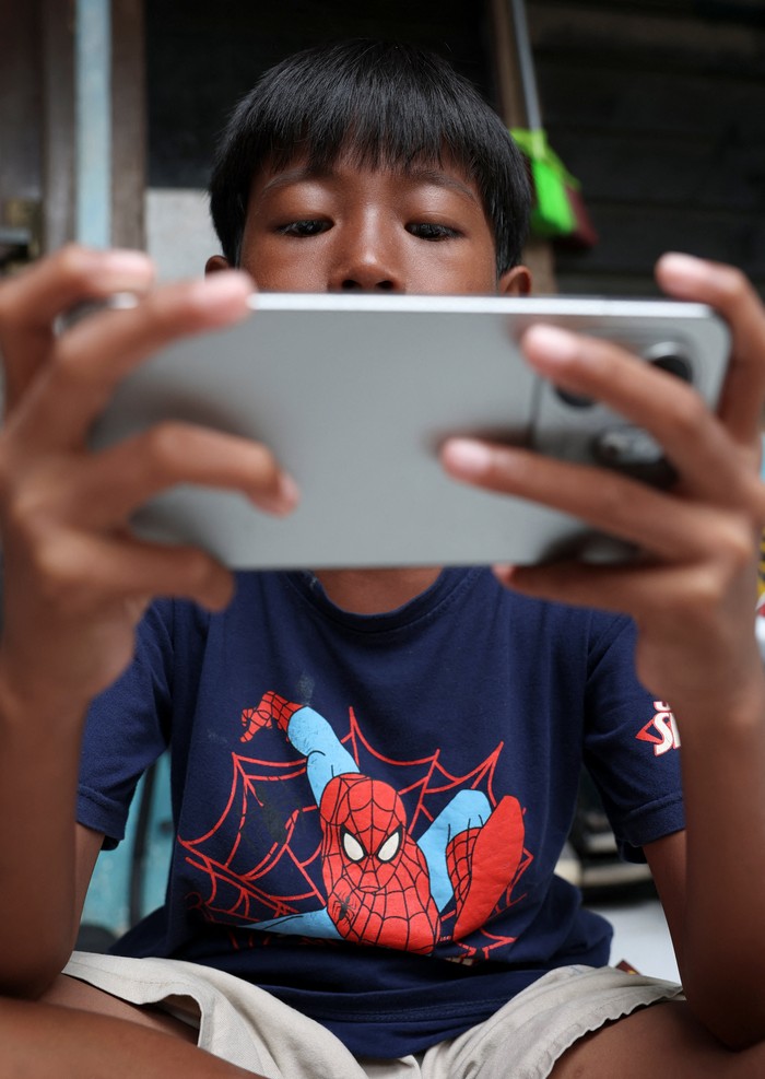 Affan Haritsah, 11, Daffa Ibnu Alkhalifi, 12, and Kevin Prince, 14, use their phones, as Indonesias communications and digital information ministry implements restrictions against high-risk social media platforms, including Facebook, TikTok, and R