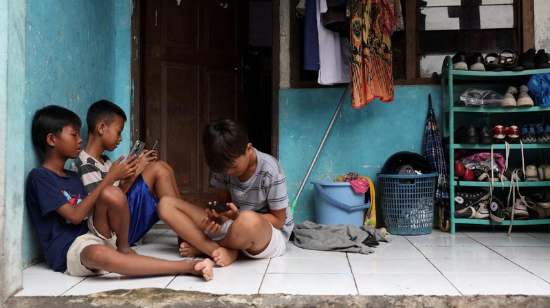 Affan Haritsah, 11, Daffa Ibnu Alkhalifi, 12, and Kevin Prince, 14, use their phones, as Indonesia's communications and digital information ministry implements restrictions against 