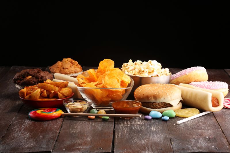 Woman reaching for a donut from a table full of junk food, showing signs of sugar cravings, overeating, and unhealthy eating habits