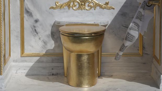 A statue featuring a large golden toilet, titled 