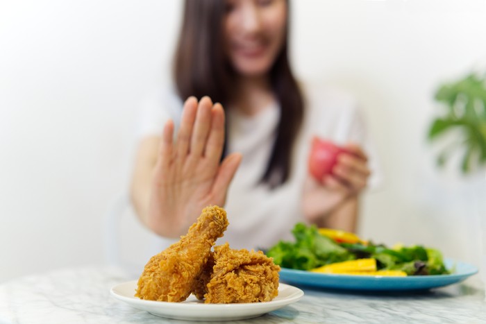 Young girl on dieting for good health concept. Close up female using hand reject junk food by pushing out her favorite fried chicken and choosing red apple and salad for good health.