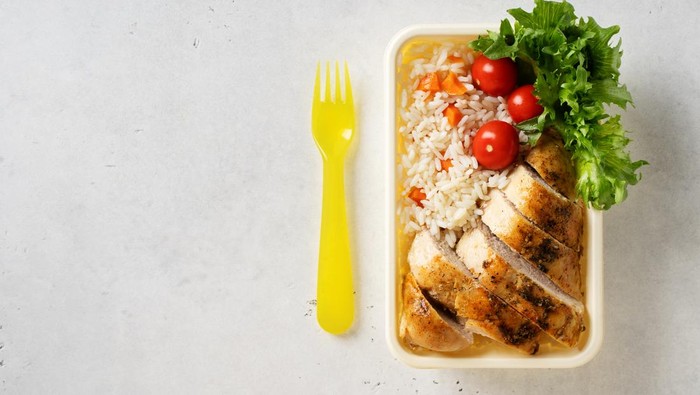 Lunch box with chicken, rice, vegetables, tomatoes, salad, fruits and nuts on white background, top view