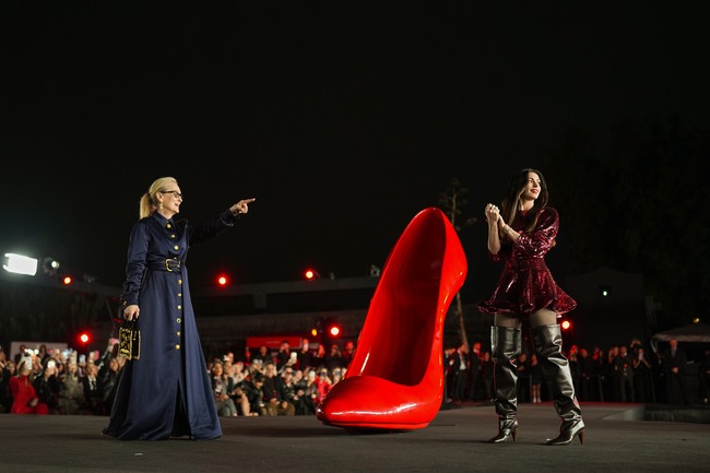 Meryl yang kembali memerankan karakter ikonik Miranda Priestly, tampil elegan dalam balutan coat navy berpotongan tegas dari Schiaparelli. Mantel tersebut dilengkapi detail kancing emas berukir di bagian depan, menciptakan kesan mewah sekaligus powerful. Ia memadukannya dengan anting drop emas serta tote bag hitam-emas berstruktur dari label yang sama. (Foto: Angel Delgado/Getty Images for Disney)