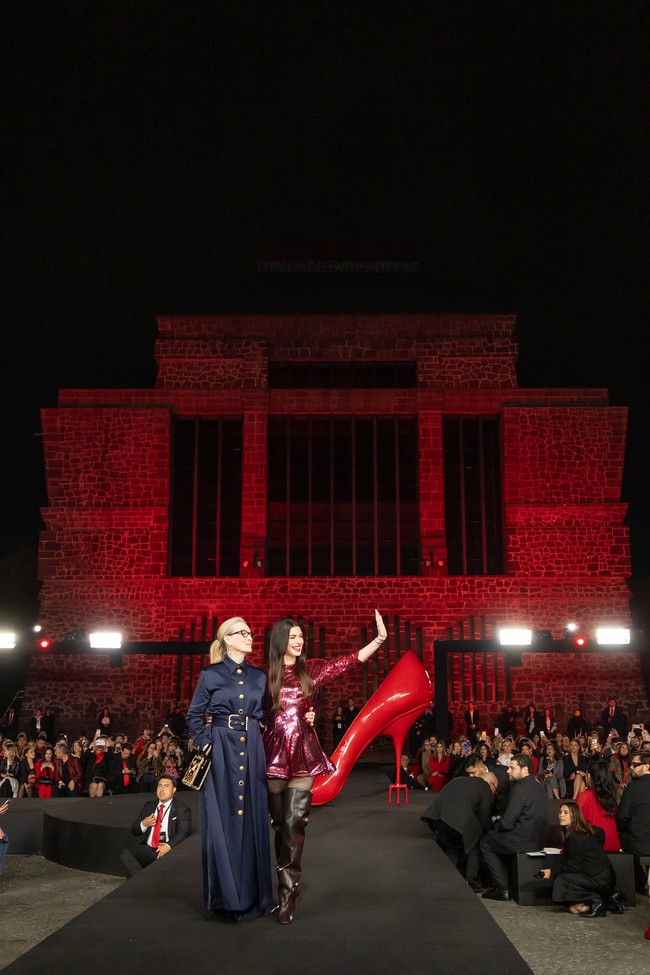 Sementara itu, Anne Hathaway tampil kontras dengan gaya lebih playful namun tetap bold. Ia mengenakan mini dress berwarna pink penuh sequin dari Stella McCartney koleksi Fall 2026. Siluet rok mengembang dipadukan dengan thigh-high boots cokelat tua berdesain chunky, memberikan sentuhan edgy. Hathaway melengkapi penampilannya dengan gelang perak dan lipstik merah terang yang mencuri perhatian. (Foto: Angel Delgado/Getty Images for Disney)