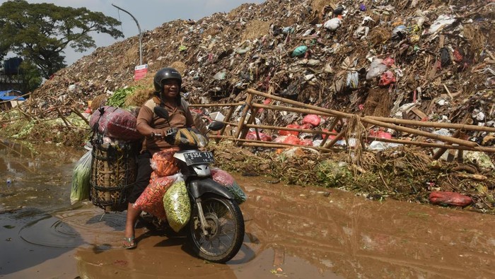 Buruh angkut berjalan di dekat tumpukan sampah yang meluber di Tempat Pembuangan Sementara (TPS) Pasar Induk Kramat Jati, Jakarta, Kamis (2/4/2026).  Penumpukan disebabkan karena pembatasan kuota pengiriman sampah ke TPST Bantar Gebang pascainsiden longsor di lokasi tersebut pada 8 Maret 2026 lalu. ANTARA FOTO/Indrianto Eko Suwarso/wsj.