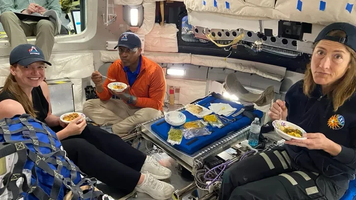 Astronaut NASA Victor Glover (tengah) dan Christina Koch (kanan) mencoba makanan luar angkasa di simulator kapsul Orion