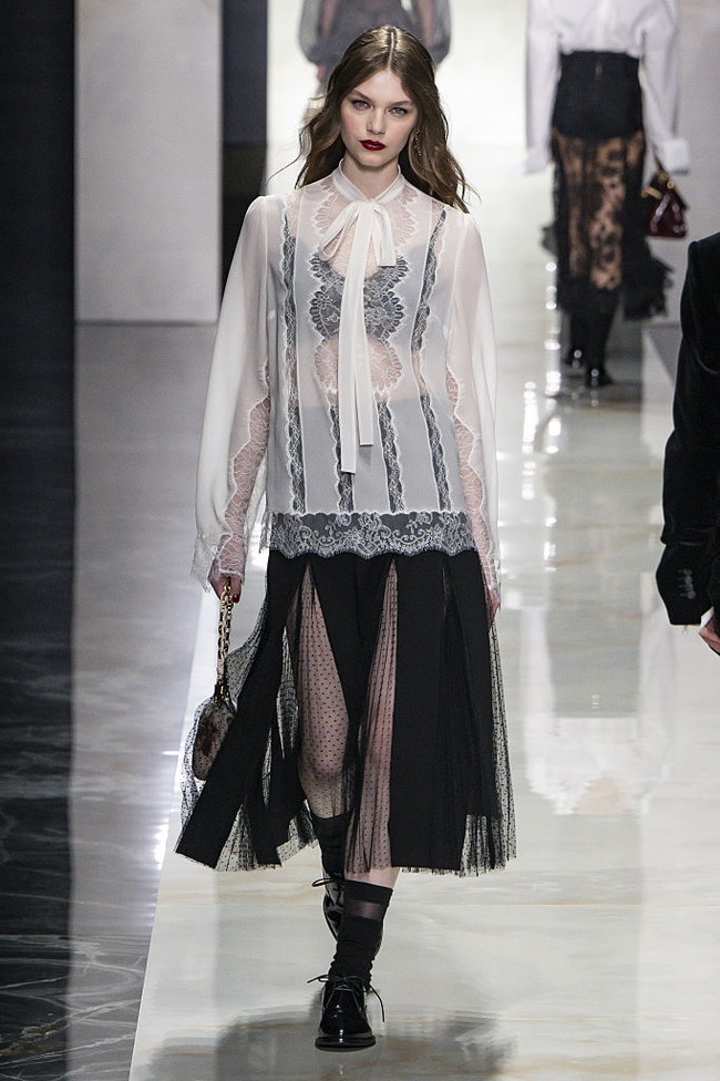 Koleksi ini juga menonjolkan sensualitas dalam bentuk yang lebih subtil. Inspirasi dari Sisilia klasik dihadirkan melalui dominasi warna hitam, putih, shawl, serta teknik crochet tradisional. Renda menjadi elemen kunci, membingkai tubuh dengan efek transparan, permainan antara tertutup dan terbuka, serta potongan leher rendah yang elegan. (Foto: Victor VIRGILE/Gamma-Rapho via Getty Images)