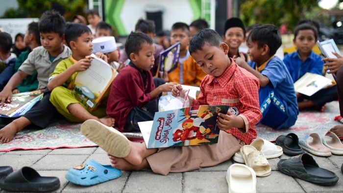 Sejumlah anak membaca buku dongeng di Kampung Pekijing, Kota Serang, Banten, Sabtu (4/4/2026). Kegiatan lapak baca dan permainan tradisional yang rutin diselenggarakan pada Sabtu-Minggu dan diinisasi oleh pemuda setempat tersebut menjadi wujud nyata dukungan warga terhadap Peraturan Pemerintah (PP) Tunas terkait pembatasan media sosial pada anak, sekaligus dinilai efektif dalam menekan kecanduan gawai. ANTARA FOTO/Muhammad Bagus Khoirunas/YU