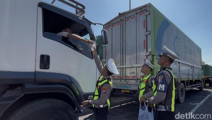 Petugas satlantas Polresta Banyuwangi membagikan nasi bungkus dan air mineral kepada pengemudi truk di kantung parkir Bulusan, Banyuwangi.